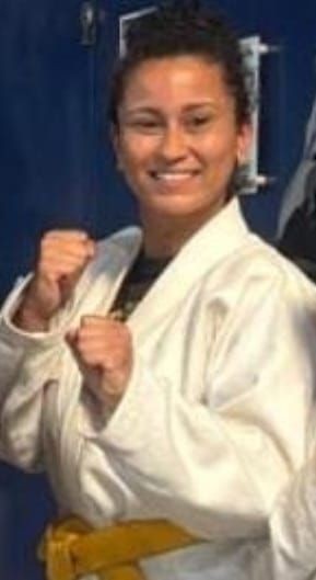 Person in a martial arts uniform with a yellow belt, smiling and posing with fists raised.